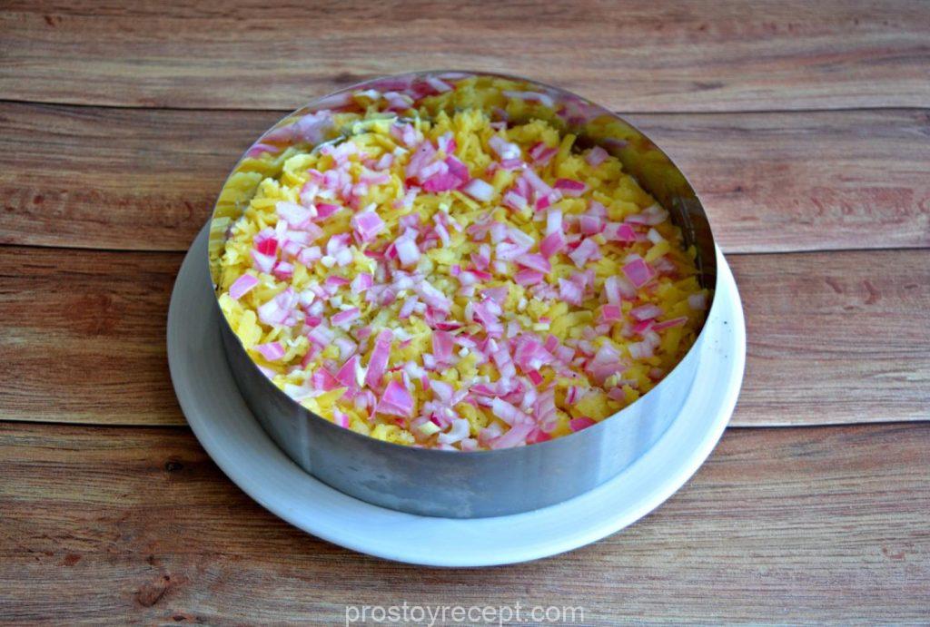 Завершите композицию, деликатно распределив оставшийся маринованный лук по поверхности картофельного