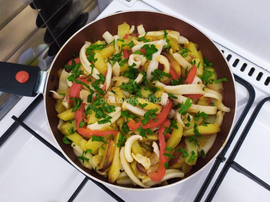 Посыпьте картофель с кальмарами нарубленной зеленью и снимите сковороду с